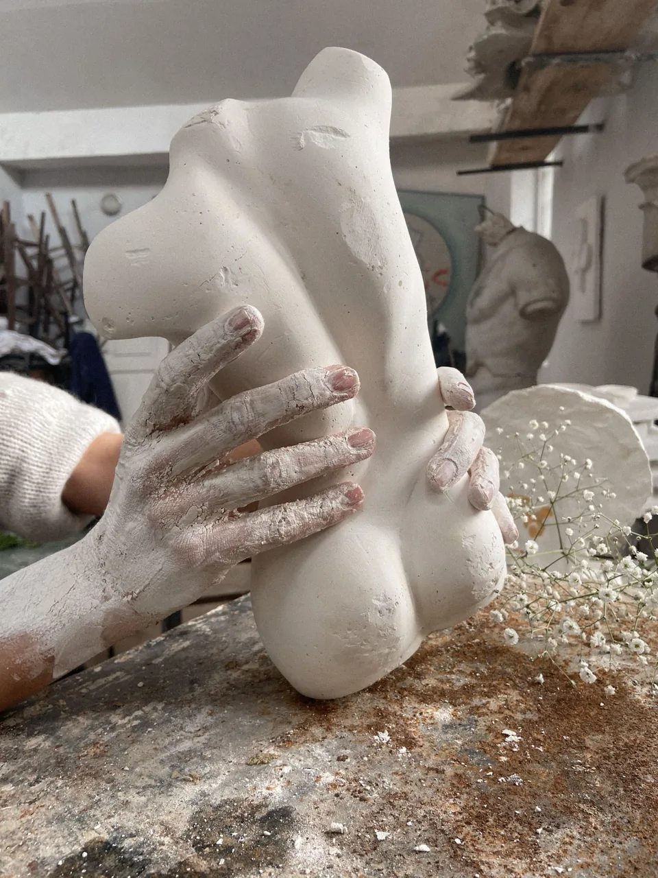 Clay-covered hands shaping a sculpture in an artist’s workshop